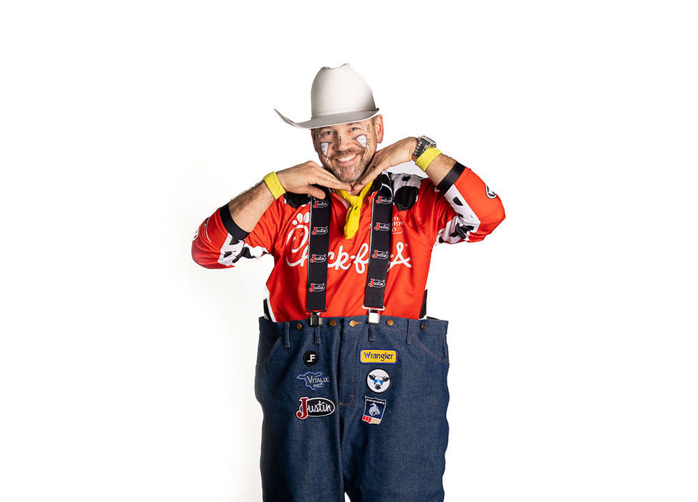 El barrendero profesional Matt Merritt, vestido con una camisa roja, un sombrero de vaquero blanco y sonriendo, con las manos debajo de la barbilla, tratando de verse lindo.